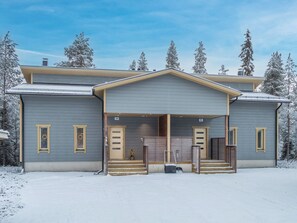 Un edificio de dos pisos con un porche cubierto y un camino de entrada cubierto de nieve.