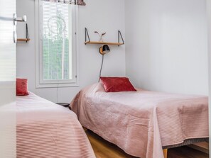 A bedroom with two single beds, a window with blinds, a wall-mounted shelf with a lamp, and a red pillow on one bed. - Saukonpesä a by Interhome (Kuusamo)