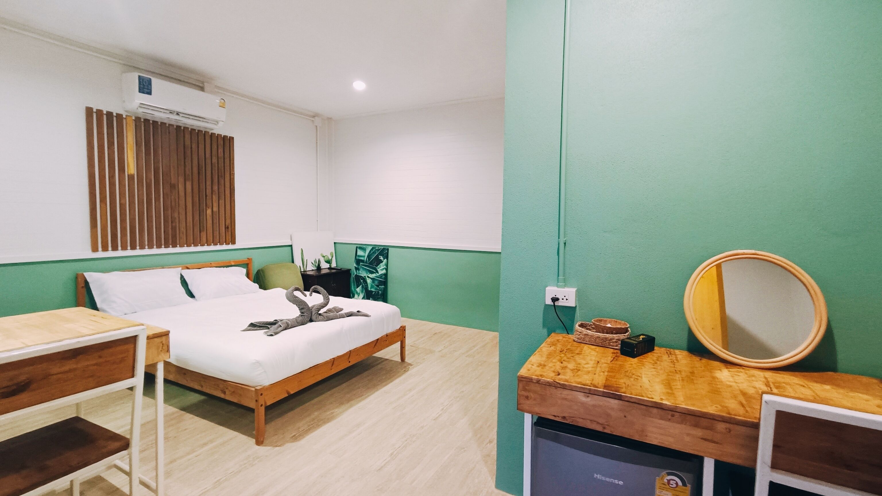A room with a bed, a wooden desk, a mirror, and a small table.
