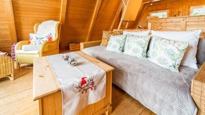 A cozy, wooden-furnished room with a bed, a wicker chair, and a small table with a decorative cloth.