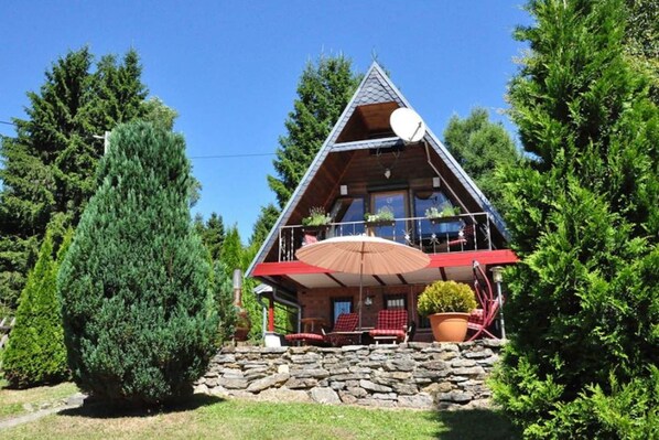 Une cabane avec des fondations en pierre, un balcon avec des chaises rouges et une antenne parabolique.