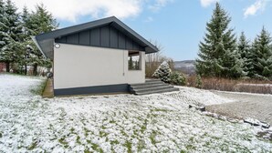 Ein modernes Haus mit geneigtem Dach, einer kleinen Veranda und einer Treppe, die zum Eingang führt.