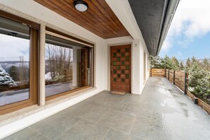 Enter a serene space with a large sliding glass door leading to a covered porch with a tiled floor and wooden railing.
