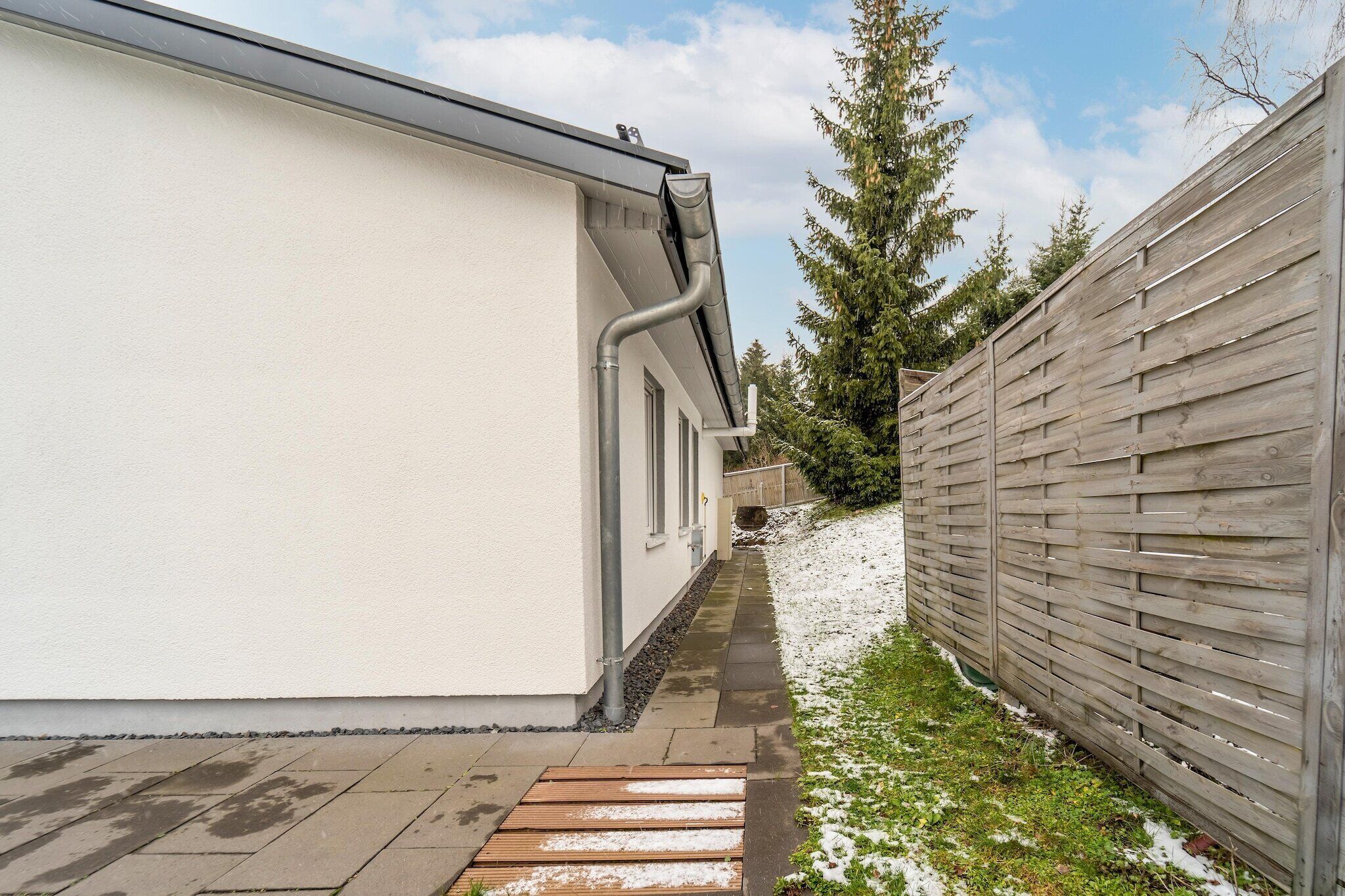 Un étroit sentier mène à un bâtiment à l’extérieur blanc, bordé d’une clôture en bois d’un côté.