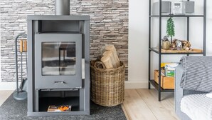 A modern living room with a stone wall, a gray fireplace with a glass door, a wicker basket, and a shelf with various items.