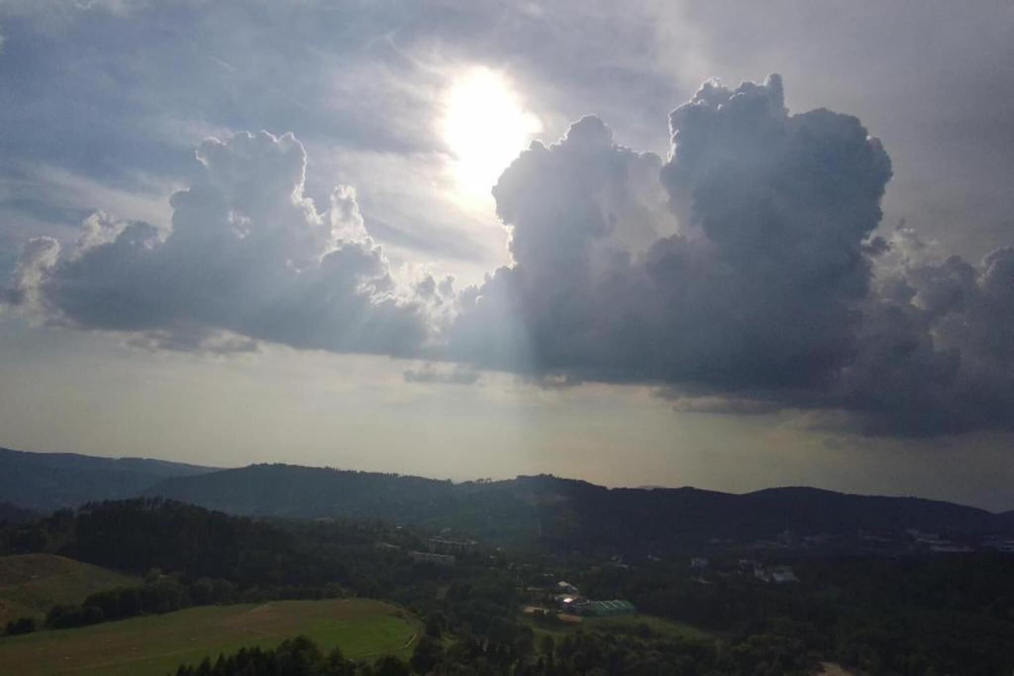 A landscape with a sun shining through clouds, a valley with fields, and distant hills.