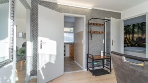 A modern interior with a wooden floor, a patterned wall, a door leading to a kitchen, and a framed picture on the wall.