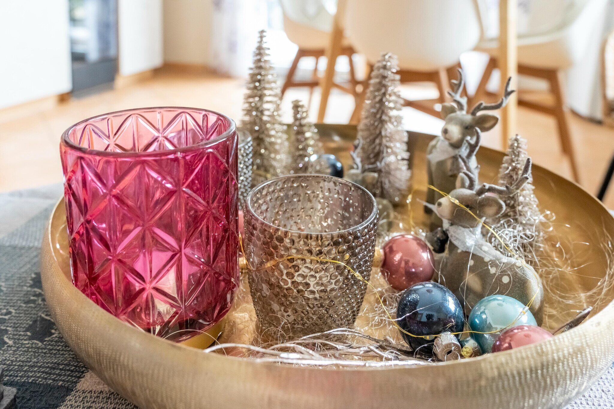 A decorative tray with a pink glass, a textured glass, and various ornaments including a reindeer and Christmas trees.