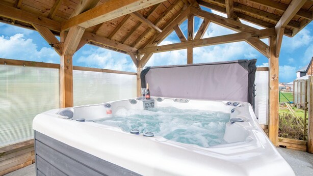 Un jacuzzi bajo una pérgola de madera con cielo despejado.