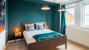 Un dormitorio con cama, dos lámparas de noche, una mesita de noche y una ventana con cortinas.