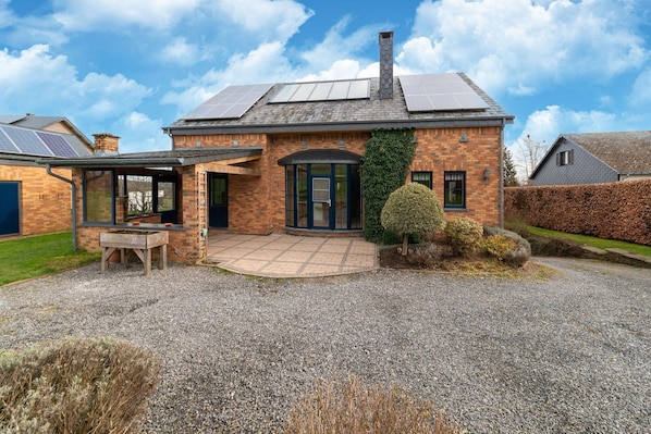 Une maison avec une façade en briques, un patio couvert, une cheminée et des panneaux solaires sur le toit.