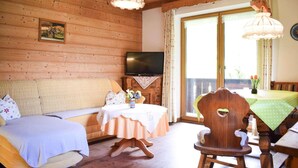 Une pièce chaleureuse avec un décor intérieur en bois, un canapé, une table à manger avec des chaises, un téléviseur et une fenêtre avec des rideaux.
