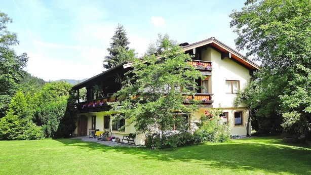 Une maison à deux étages dotée d’un balcon, entourée d’une végétation luxuriante et d’une pelouse bien entretenue.