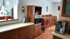 A kitchen with wooden cabinets, a built-in oven, a coffee machine, and a window with lace curtains. - Spacious holiday home in Piechowice with garden (Piechowice)