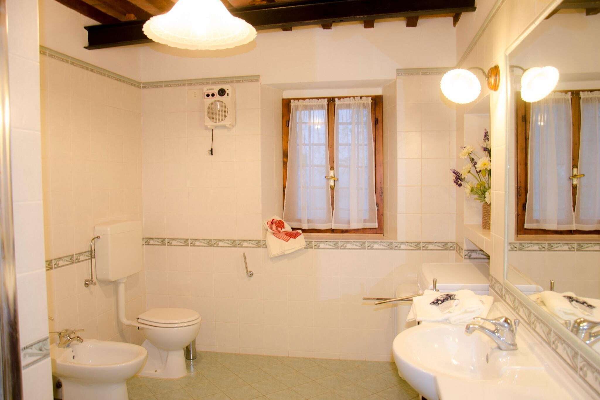 A bathroom with a toilet, bidet, and sink. There is a window with curtains, a mirror, and a towel rack.