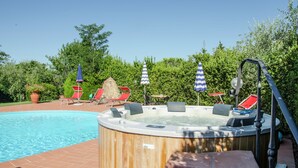 Un jacuzzi con sillones reclinables rojos, una piscina y sombrillas.