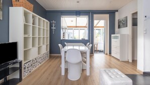 A modern dining area with a white table and chairs, a white shelving unit, and a television on a stand. - Cosy cottage a stone's throw from Cap Gris Nez (Audinghen)