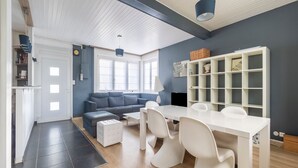 A modern living room with a sofa, dining table, and chairs. There is a bookshelf and a fireplace. - Cosy cottage a stone's throw from Cap Gris Nez (Audinghen)