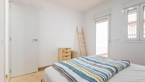 A bedroom with a bed, a wooden ladder, a small wooden cabinet, and a window.