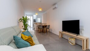 A modern living room with a sofa, a TV, and a dining area in the background.