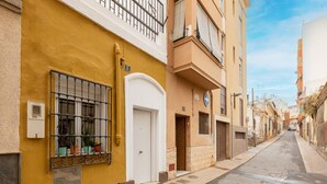 A narrow street with yellow and beige buildings, a white door, and a window with potted plants.