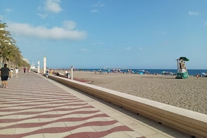 Una playa con un paseo de baldosas, palmeras y una torre de salvavidas.