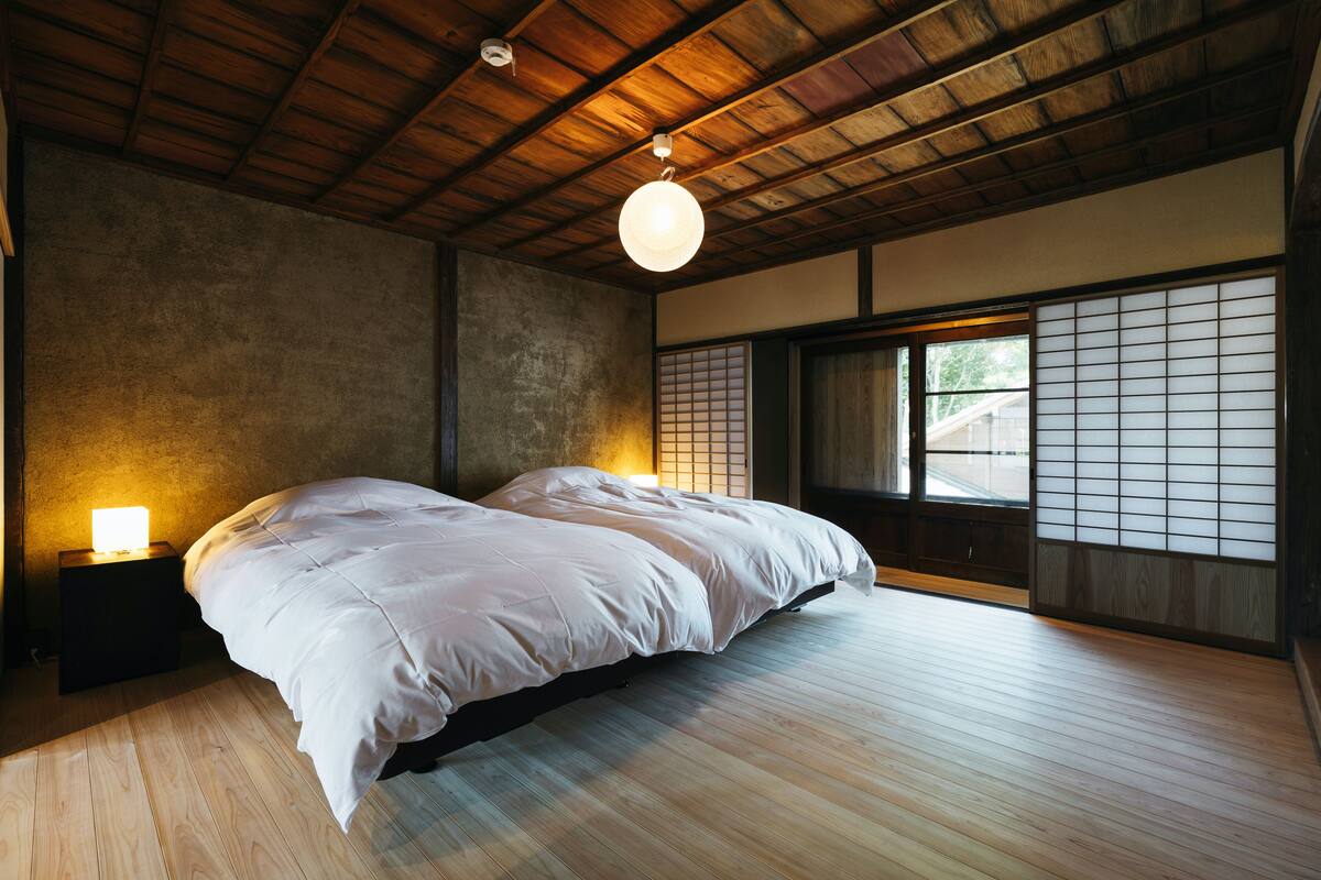 Ein Schlafzimmer mit einem großen Bett, Holzböden, einem Nachttisch mit Lampe und einer Shoji-Schiebetür.