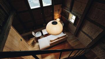 A high-ceiling room with a wooden floor, a round woven light fixture, a sofa, and a chair.
