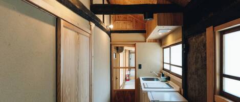 A narrow hallway with wooden walls and a wooden ceiling. There is a small kitchen area with a refrigerator, sink, and cabinets.