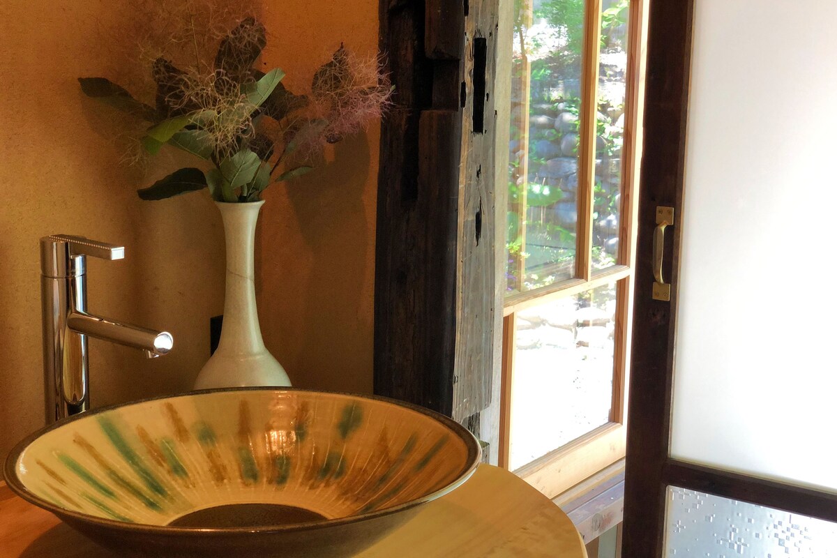Un bagno con un lavandino bianco, un rubinetto cromato e un vaso con piante essiccate.
