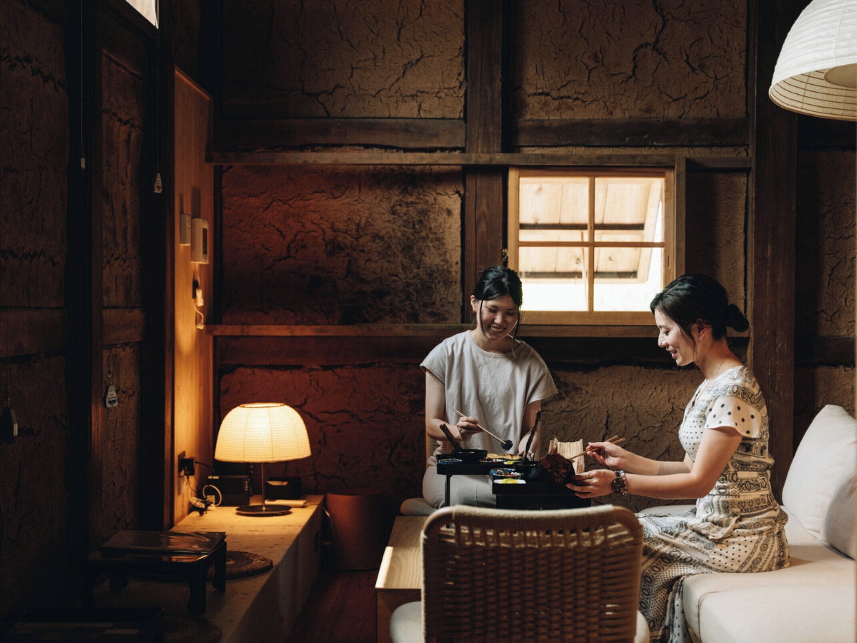 A cozy room with a wooden interior, a table with a lamp, and two people dining.