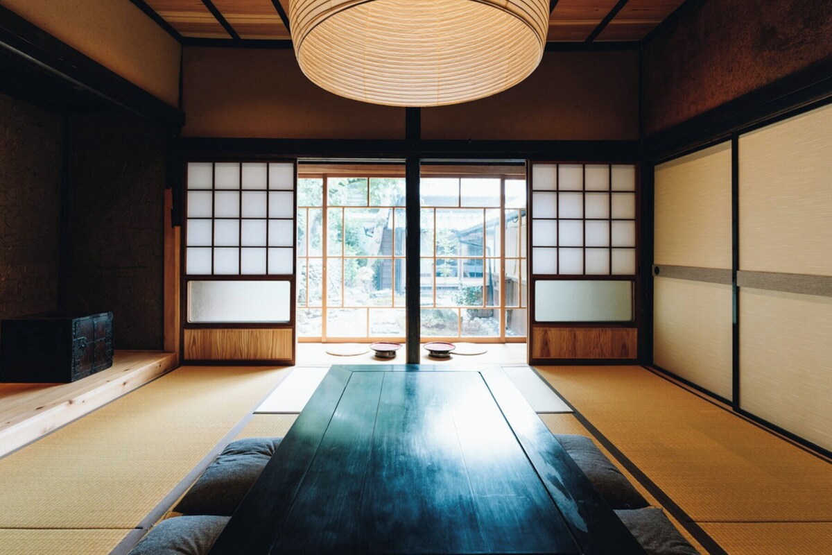 Um quarto japonês tradicional com tatames, uma mesa baixa, portas deslizantes e um lustre.