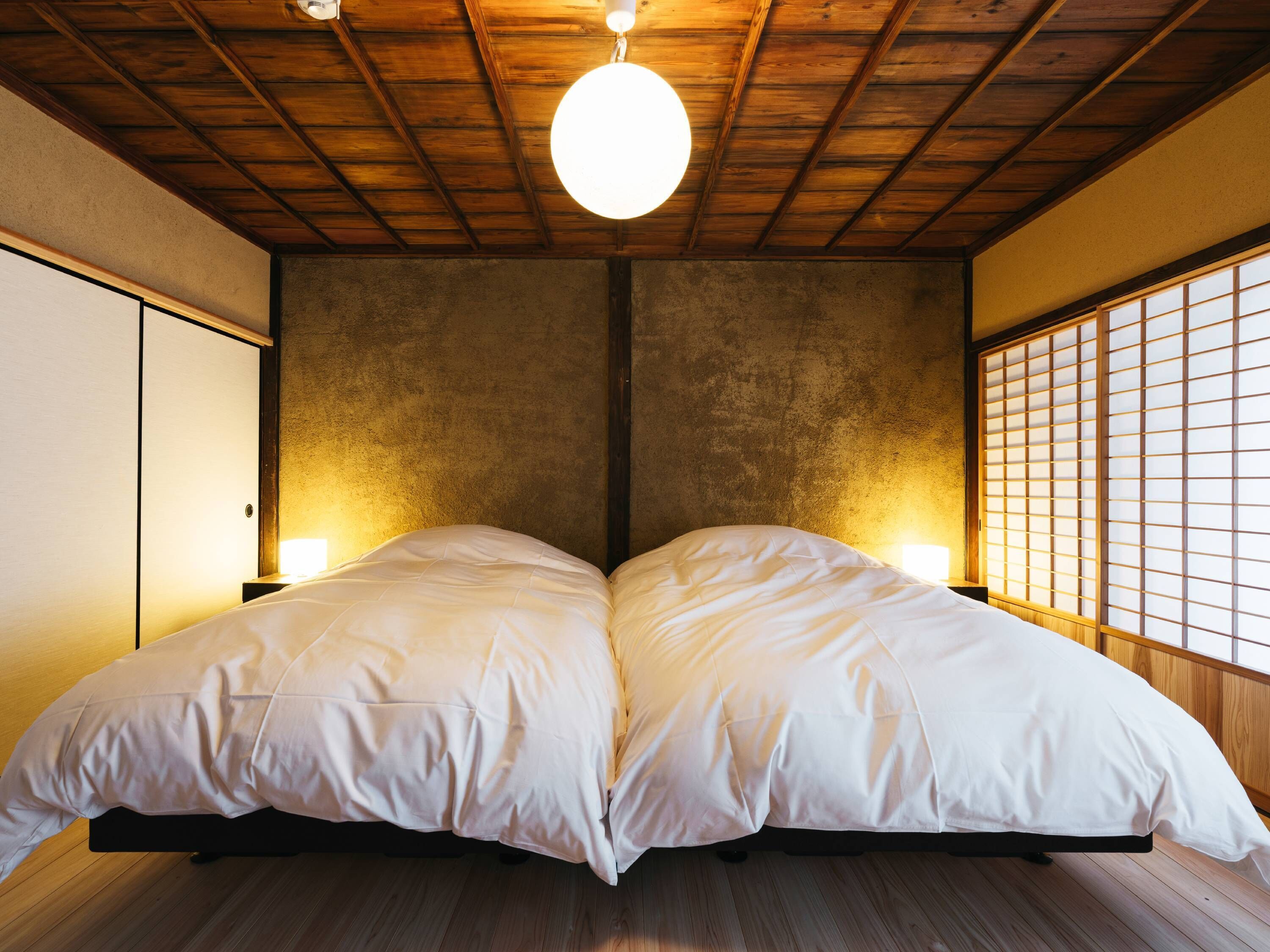 A room with a wooden ceiling, a bed with white bedding, and a traditional Japanese shoji screen on one wall.