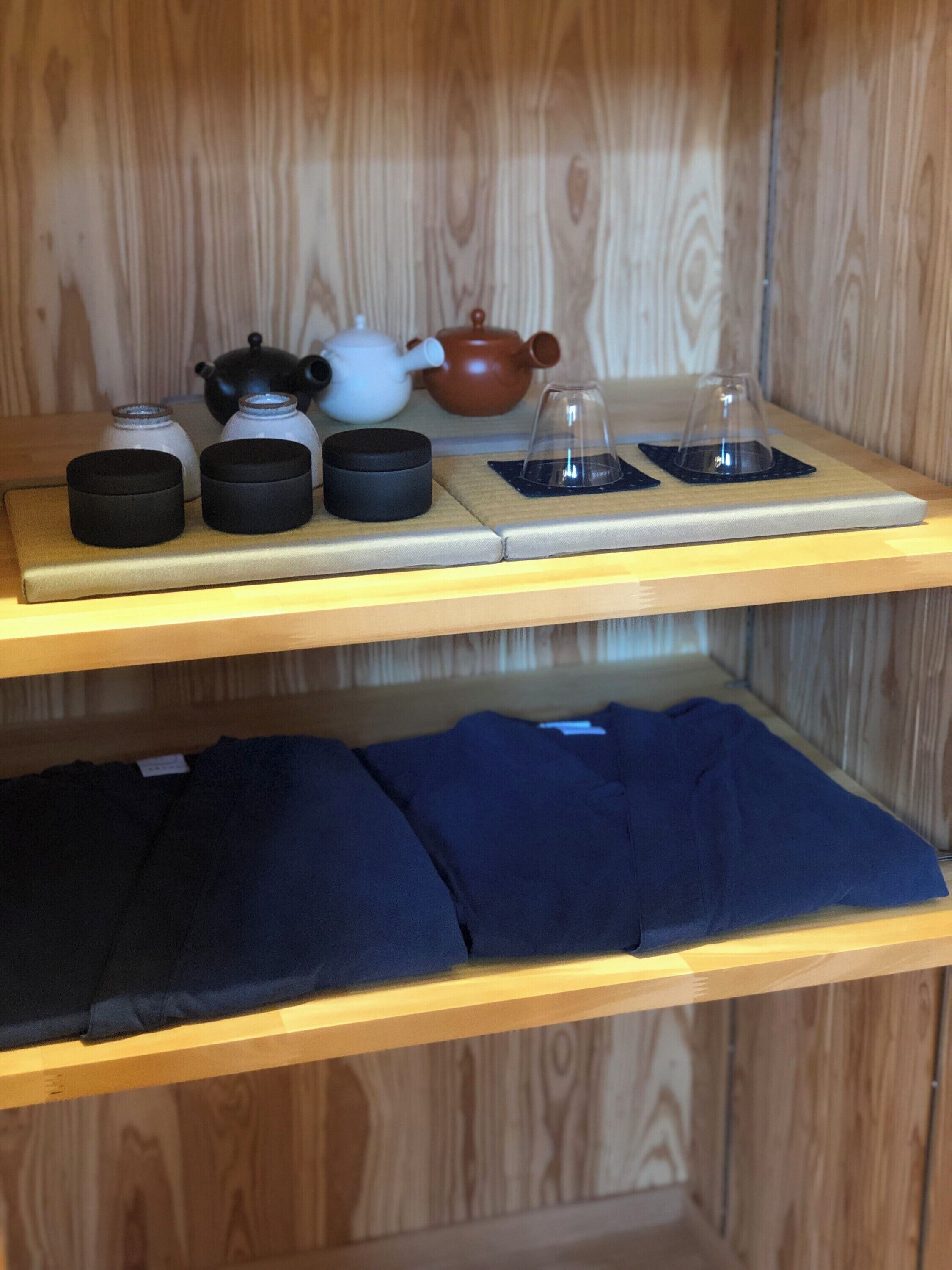 A shelf with tea sets and a folded blue garment.