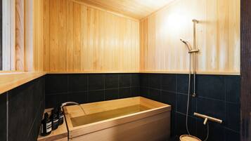 Una bañera de madera con ducha, un banco de madera y baldosas negras.