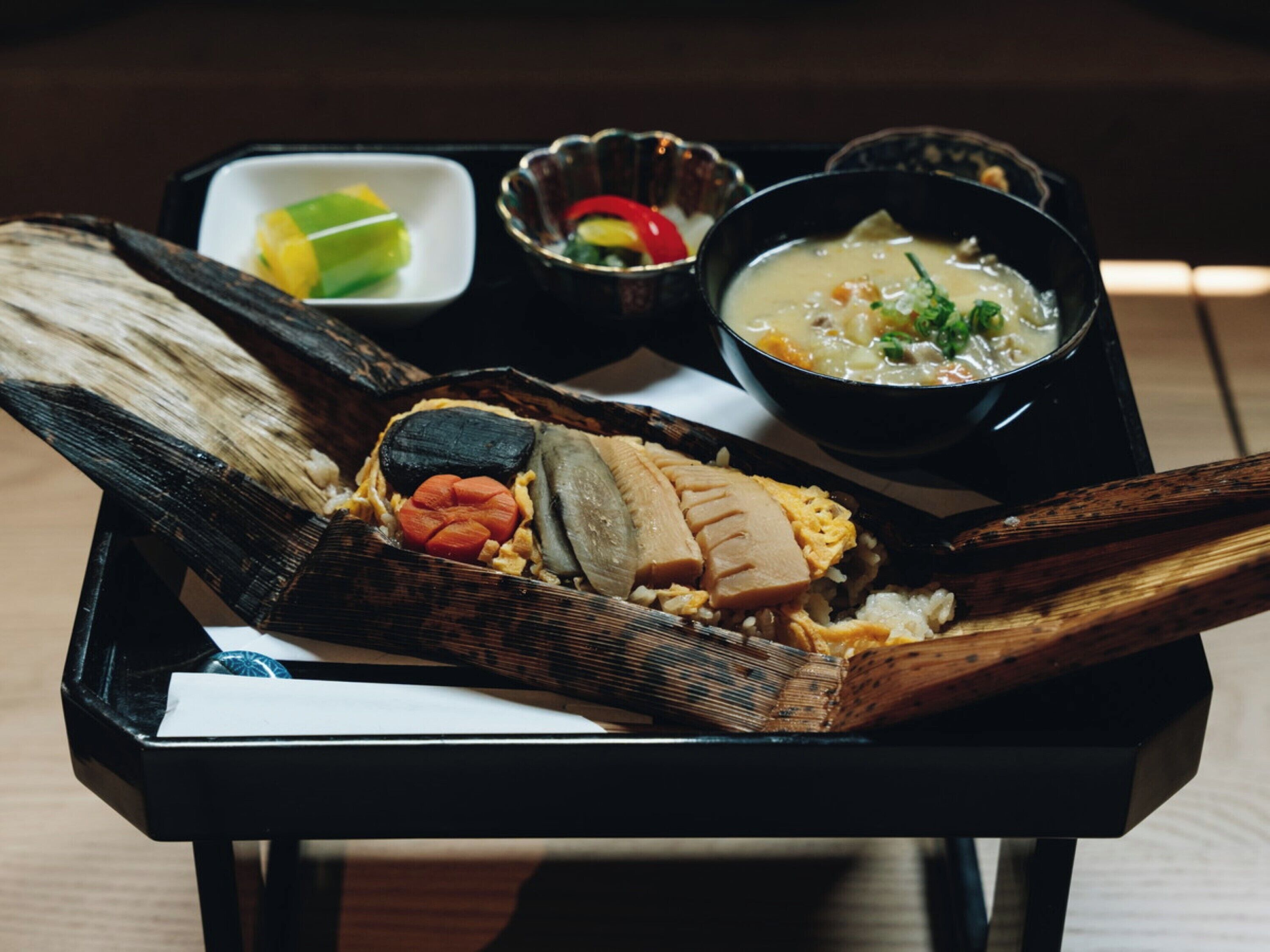 Un pasto tradizionale giapponese servito su un vassoio nero, composto da sushi, sashimi e una ciotola di zuppa.