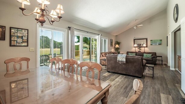 A spacious living room with a dining area, large windows, and a chandelier. - Litchfield Country Club Cottage 4BR 4BA Retreat (Pawleys Island)