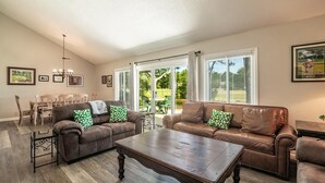 A living room with two brown leather sofas, a wooden coffee table, and a dining area with a wooden table and chairs. - Litchfield Country Club Cottage 4BR 4BA Retreat (Pawleys Island)