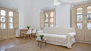 Un salón espacioso con un sofá blanco, una mesita redonda con una planta y una zona de comedor con sillas.