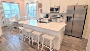 Une cuisine moderne avec des meubles blancs, un grand îlot central doté de tabourets, des appareils en acier inoxydable et un parquet en bois disposé en chevrons.