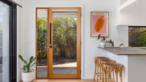 Una cocina moderna con puerta de madera que da a un jardín, una zona de bar con taburetes y un cuadro enmarcado con fruta.