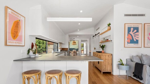 Una cocina moderna con una isla central, taburetes de madera y un comedor con sillas.