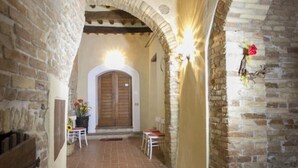 A narrow corridor with stone walls, a wooden ceiling, and a tiled floor leading to a door. - GARDEN HOUSE (San Gimignano)