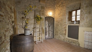 A rustic stone-walled room with a wooden barrel, a ladder, and a decorative door. - GARDEN HOUSE (San Gimignano)