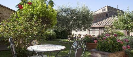 Eine Terrasse mit einem runden Tisch und Stühlen, umgeben von üppiger Vegetation und blühenden Pflanzen.