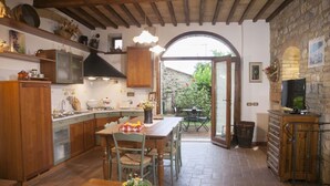 A kitchen with wooden cabinets, a dining table, and a TV on a wooden cabinet. - GARDEN HOUSE (San Gimignano)