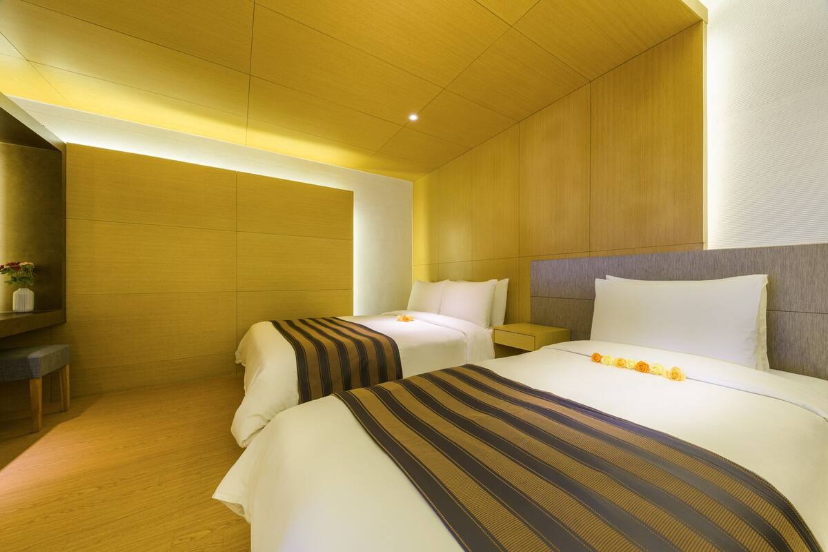 A hotel room with two beds, a wooden ceiling, and a nightstand with a lamp.