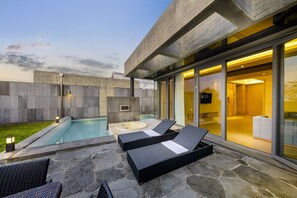 Un espace piscine extérieur moderne, doté de chaises longues et d’un jacuzzi, entouré de murs en pierre et de portes vitrées donnant accès à un espace intérieur.