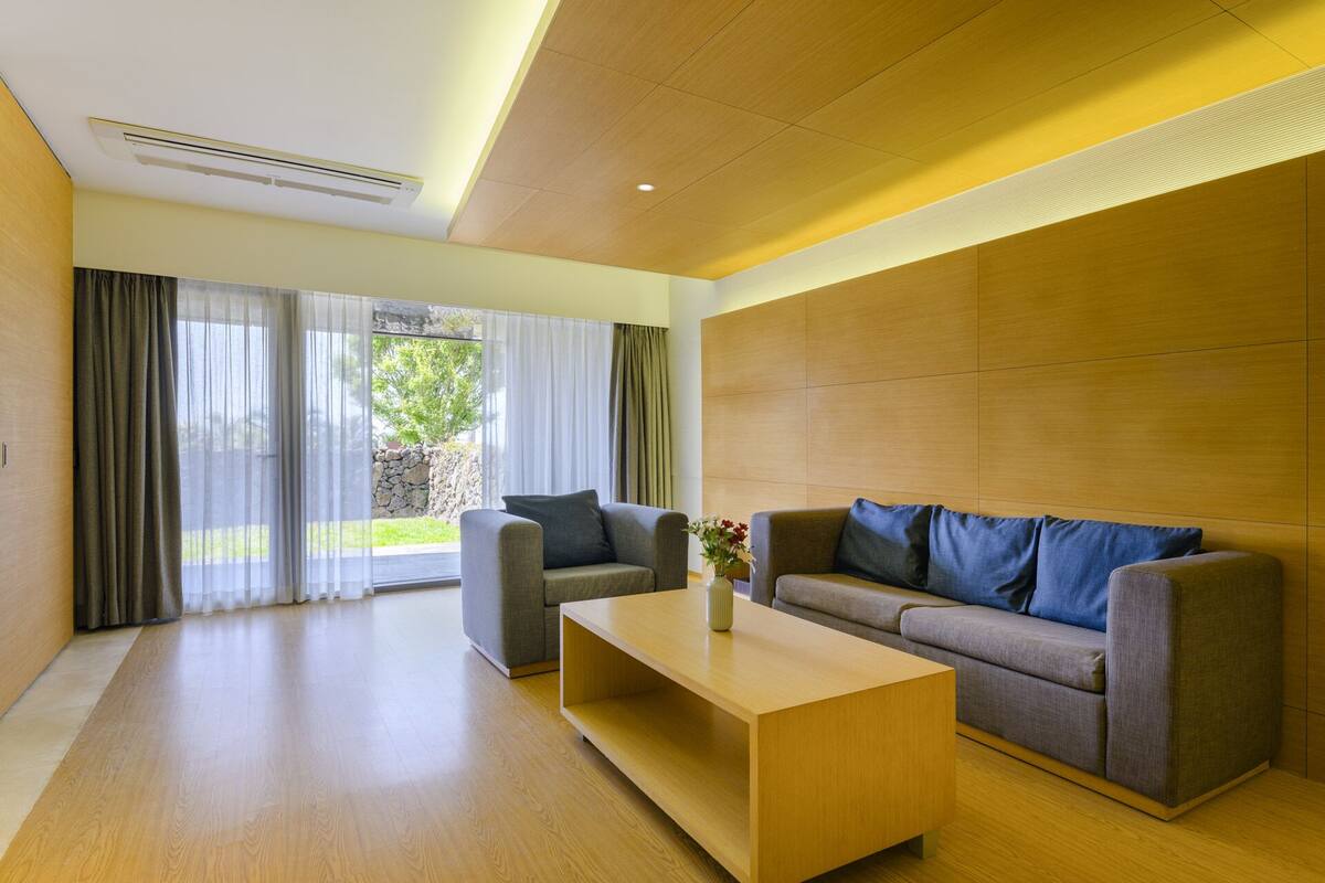 A modern living room with a sofa, a coffee table, and a large window with curtains.