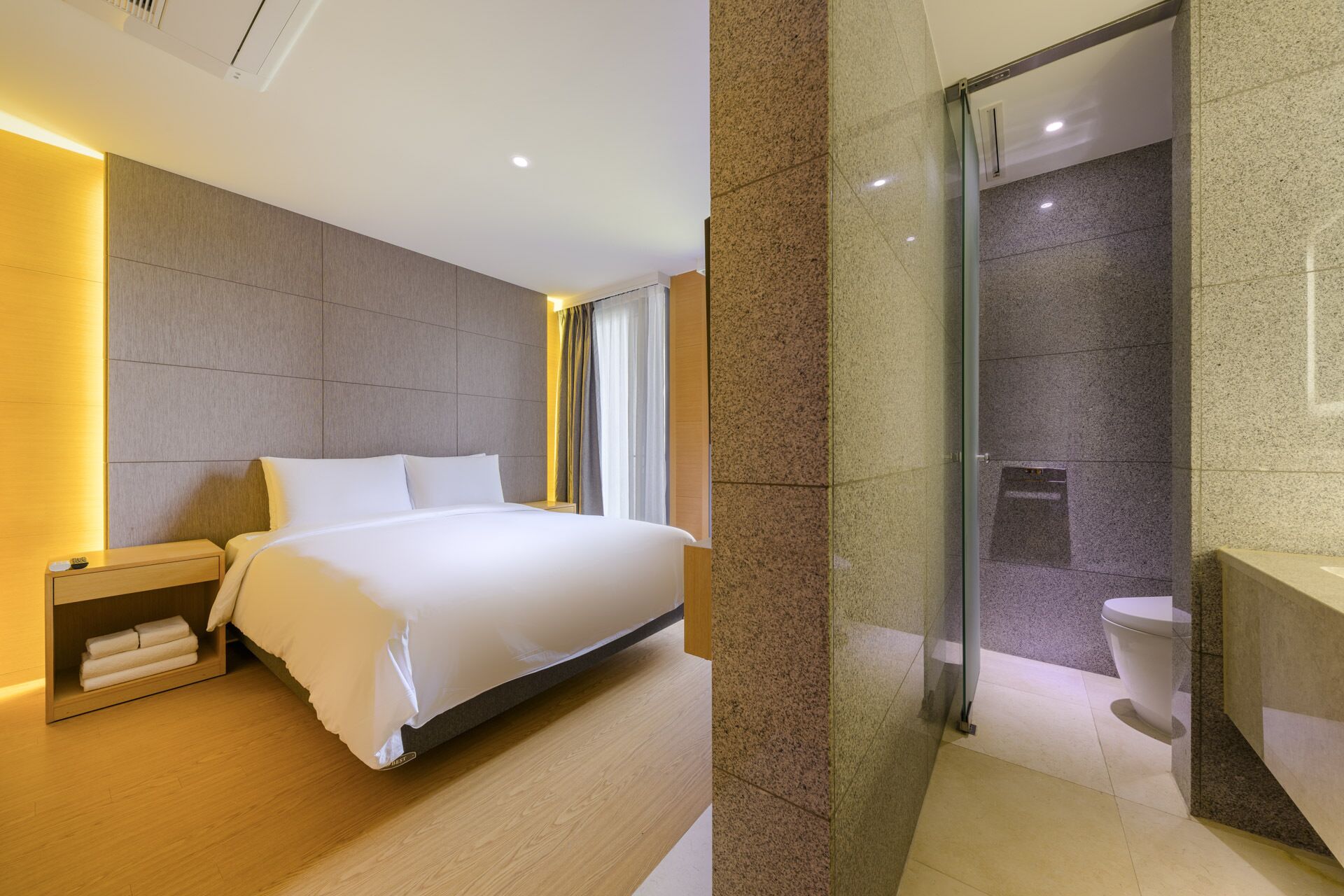 A modern hotel room with a large bed, bedside tables, a glass shower enclosure, and a visible toilet.